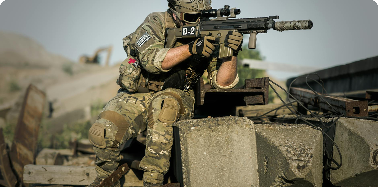 A soldier with a rifle is poised, aiming carefully at an unseen target, embodying vigilance and concentration.